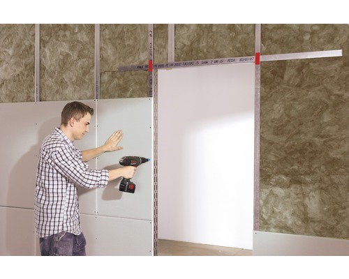 Een man bevestigt een gipsplaat met een accuschroevendraaier aan een metalen onderconstructie in een ruimte