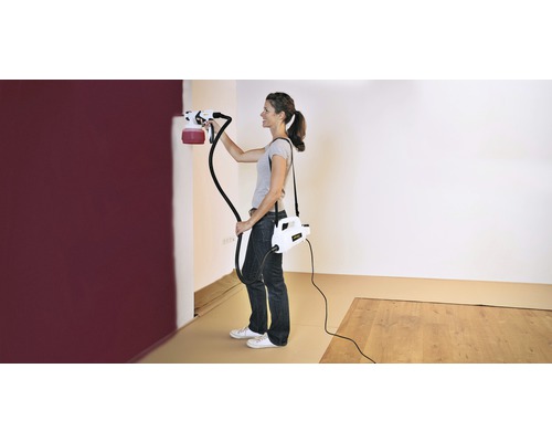 Vrouw schildert muur met verfspuitsysteem in een kamer