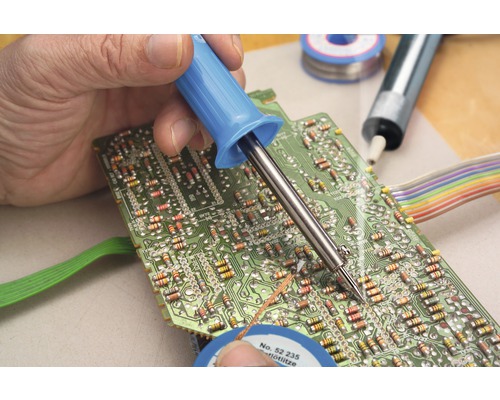 Een persoon soldeert een printplaat met een soldeerbout. Soldeertin is ook aanwezig.