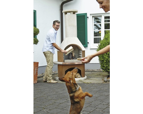 Scène met een man die hout in een tuingrill legt, terwijl een vrouw een hond een traktatie geeft.