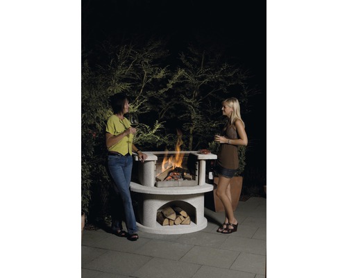 Twee vrouwen staan bij een stenen barbecue met hout en vuur.