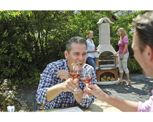 Scène met een stenen barbecue in de tuin, waar een groep mensen aan het barbecueën is en proost met wijnglazen.