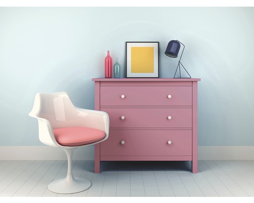 Roze commode met drie laden naast een witte kuipstoel met roze kussen, met daarop een lamp en een ingelijste afbeelding