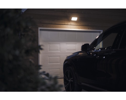 Scene met een garage, verlicht door een plafondlamp, met een auto ervoor.