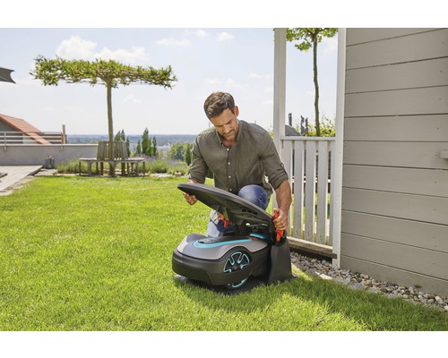 Een man opent een robotmaaier in een tuin.