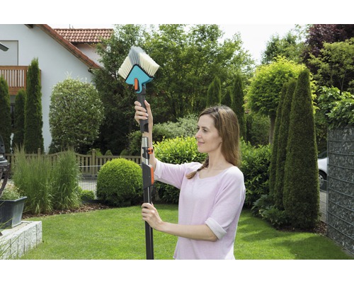 Vrouw gebruikt een wasborstel met telescopische steel voor schoonmaakwerkzaamheden in de tuin.