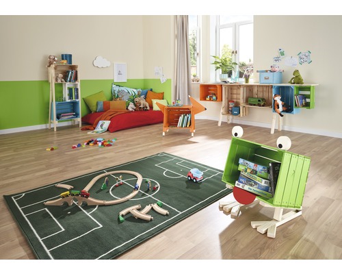 Een kinderkamer met een bed, rekken van houten kisten en een groen tapijt met voetbalveldpatroon.