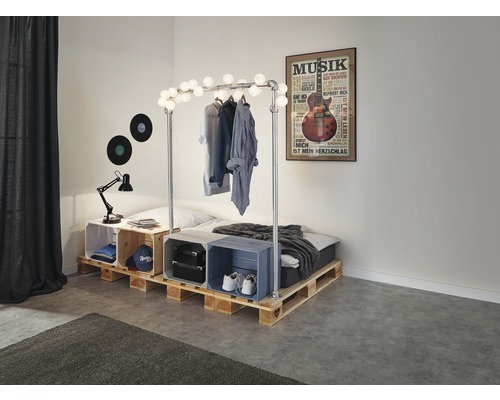 Slaapkamer met bed van houten pallets, versierd met een lichtslinger en een muziekposter