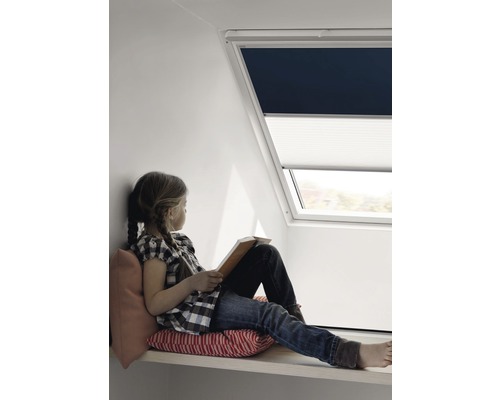 Meisje zit bij een dakraam met verduisteringsrolgordijn en honingraatplissé en leest een boek