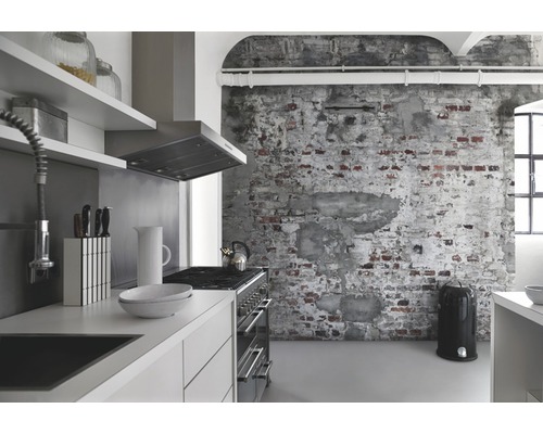 Lichte keuken met kitchenette, afzuigkap, fornuis, keukengerei en vuilnisemmer voor een bakstenen muur.