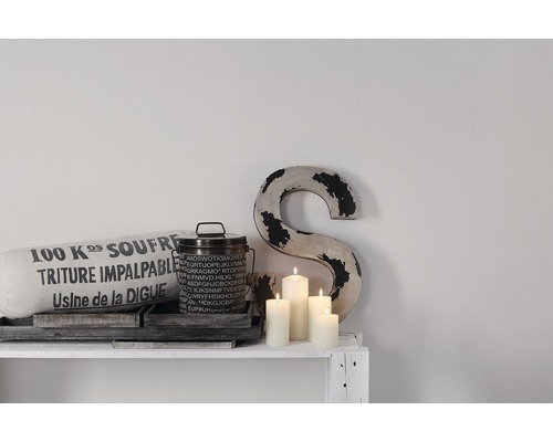 Decoratieve scène met kussen, blik, kaarsen en letterornament op een witte plank.