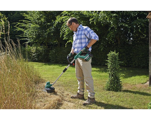 Man snijdt gras met een draadloze grastrimmer in de tuin.