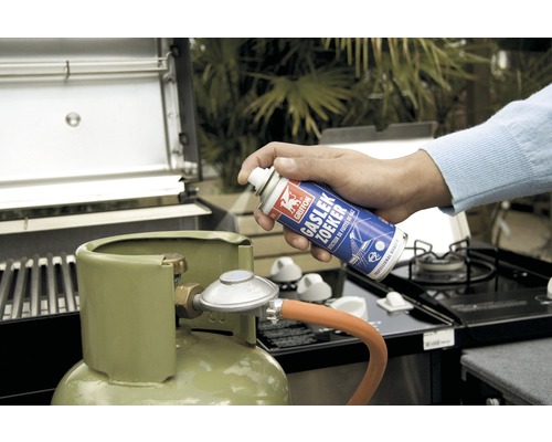Iemand test een gasfles op een barbecue met gaslekzoekspray.
