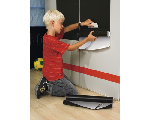 Jongen brengt zelfklevende folie aan op een kastdeur. Op de vloer ligt een rol folie en een schaar.