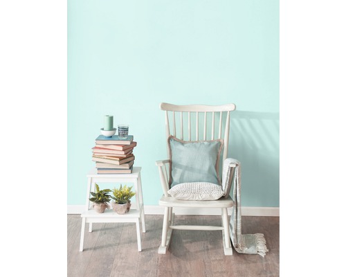 Scene met schommelstoel, bijzettafel, boeken en decoraties in een lichte kamer.