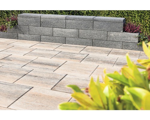 Grijze muurstenen en lichte bestrating in een buitenruimte.