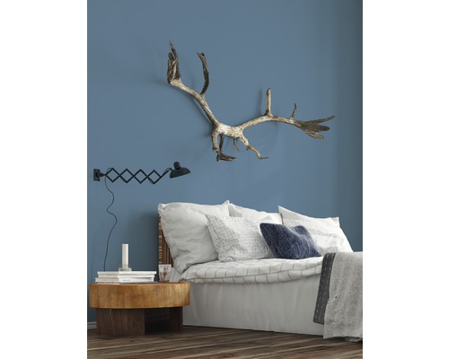 Slaapkamer met bed, nachtkastje, lamp en gewei aan de muur.