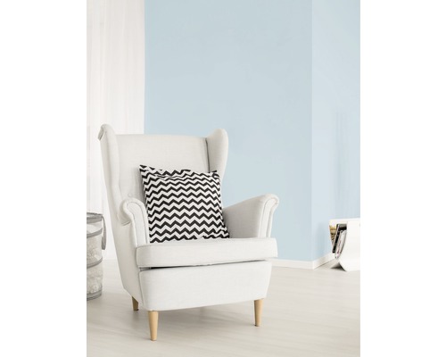 Lichte woonkamer met pastelblauwe muurverf, witte fauteuil en kussen met zigzagpatroon