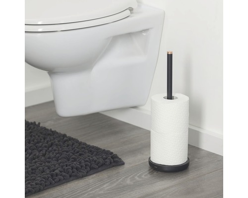 Vrijstaande toiletpapierhouder van metaal naast een toilet en een badmat