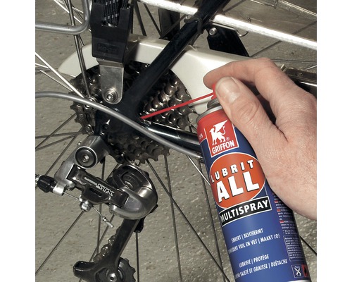 Een persoon smeert de ketting van een fiets in met een multispray.
