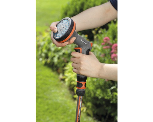 Persoon houdt een Gardena sproeier in de hand, verbonden met een tuinslang.