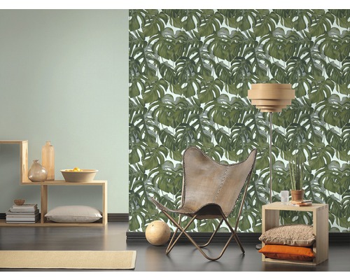 Woonkamer met Monstera blad behang, fauteuil en houten meubels voor een heldere en georganiseerde sfeer.