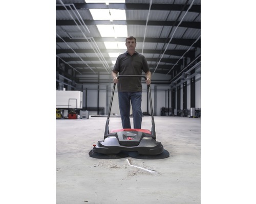 Een man bedient een veegmachine in een magazijn.