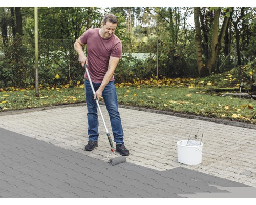 Man schildert bestrating met een verfroller en een emmer verf buitenshuis