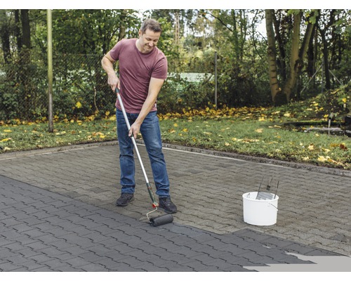 Man schildert straatstenen met verfroller buitenshuis.
