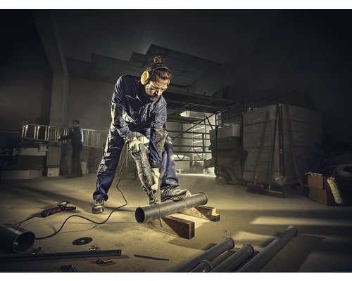 Een man zaagt een pijp met een reciprozaag in een werkplaats