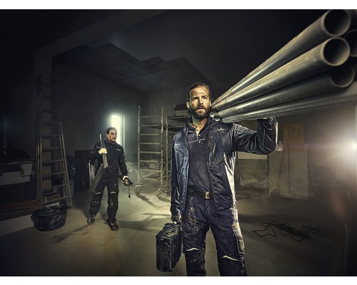Twee ambachtslieden in werkkleding vervoeren buizen en gereedschap in een heldere ruimte met ladders.