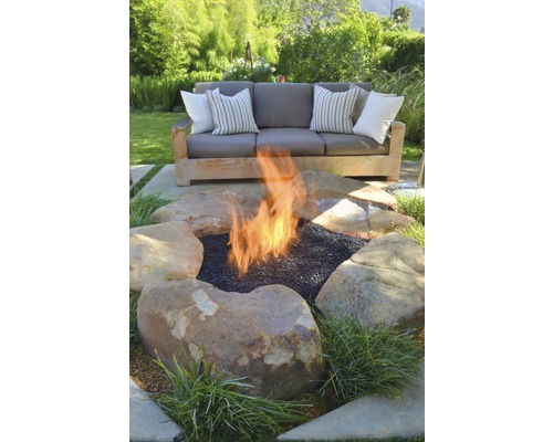 Tuinscène met vuurplaats omgeven door stenen en een bank met kussens