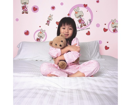 Meisje met teddybeer op een bed voor een muur met muurstickers.
