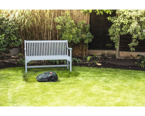 Scene met een robotmaaier voor een houten bank in een tuin.