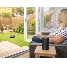 Vrouw met kopje en Amazon Echo naast robotmaaier in de tuin