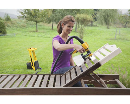 Vrouw gebruikt verfspuitsysteem om een houten ligstoel in de tuin te schilderen.