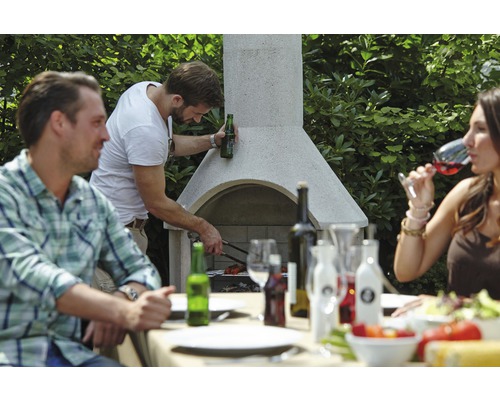 Mensen barbecueën op een tuingrill en zitten aan een eettafel
