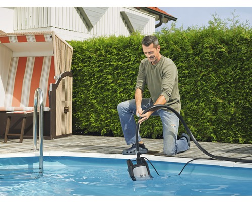 Een man bedient een dompelpomp om een zwembad in de tuin leeg te maken.