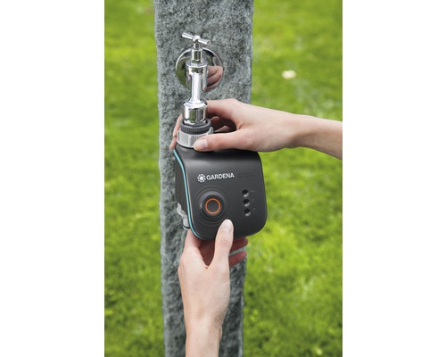 Een persoon bevestigt een Gardena Smart Water Control irrigatiecomputer aan een buitenkraan.