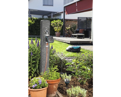 Tuinscene met waterkraan, irrigatiebediening en robotmaaier in de tuin