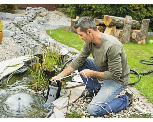 Een man gebruikt een vijverpomp in de tuinvijver met waterspel.