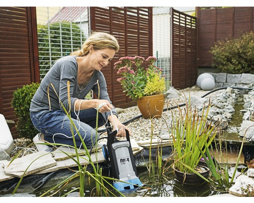 Vrouw bedient een vijverpomp van het merk for_q in een tuinvijver.
