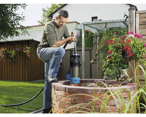 Man bedient een diepwaterpomp bij een waterput in de tuin.