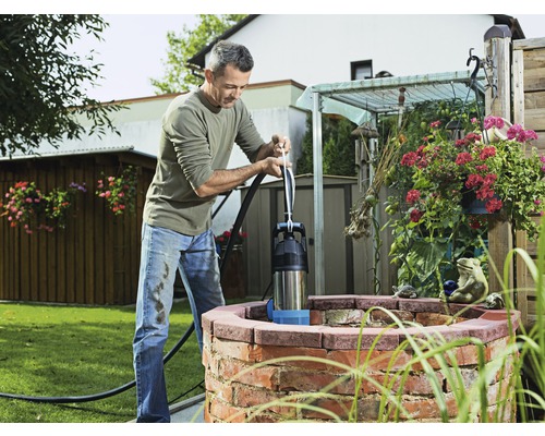 Man bedient een handpomp bij de waterput in de tuin.