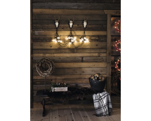 Rustieke houten wanddecoratie met geweien, lichtslingers, bank, deken en houtblokken voor een gezellige sfeer