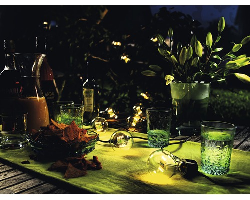 Tafel met drankjes, glazen, snacks en een lichtsnoer in de tuin ''s nachts.