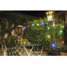 Buitenscène met groen tuinmeubilair, verlicht met een lichtsnoer en een lantaarn.