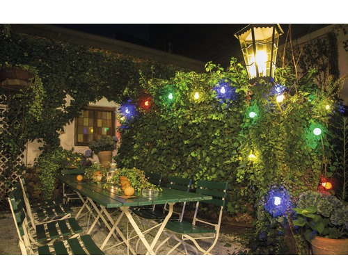 Buitenscène met groen tuinmeubilair, verlicht met een lichtsnoer en een lantaarn.