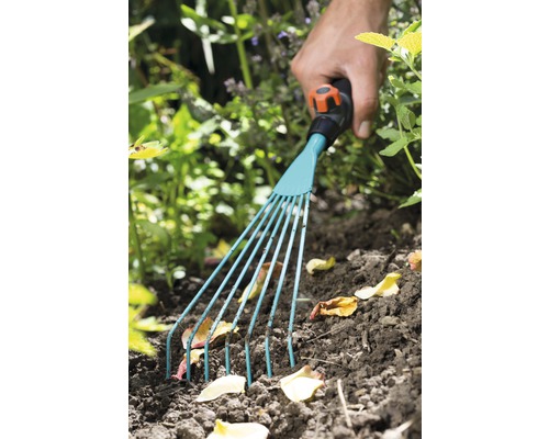 Hand met tuinhark die bladeren uit de tuinbedding verwijdert
