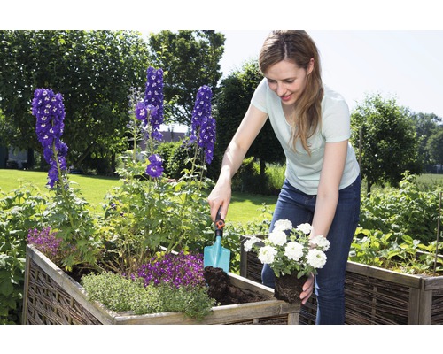 Vrouw plant bloemen in een verhoogde tuinbak in de tuin.